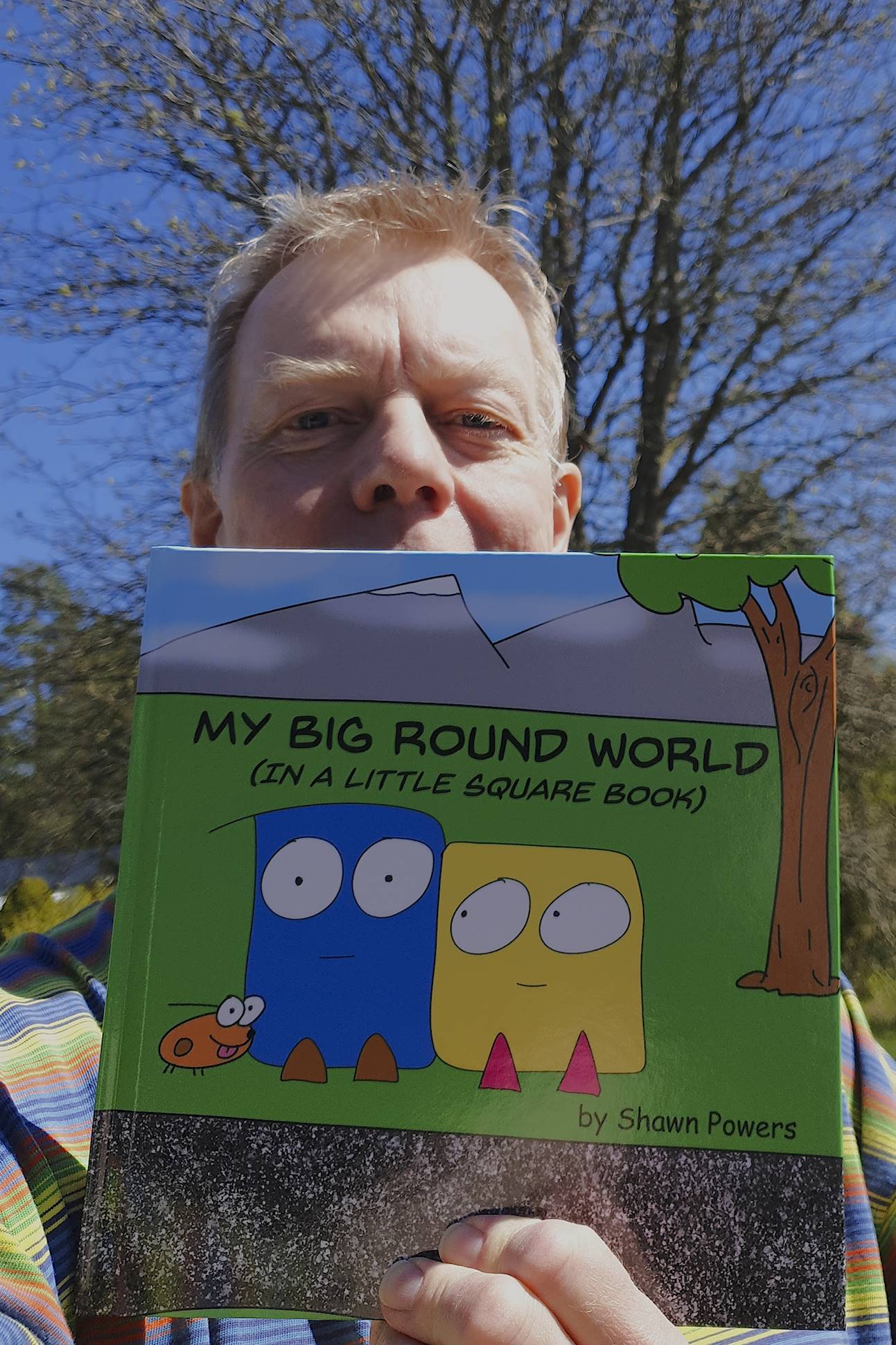I hold the book My big round world by Shawn Powers in front of me. A tree is in the background
